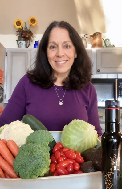 Julie Miescke smiling in her kitchen behind a bowl of fresh vegetables.